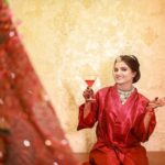 a women posing with makeup on face and wearing jewellery and drink glass in hands