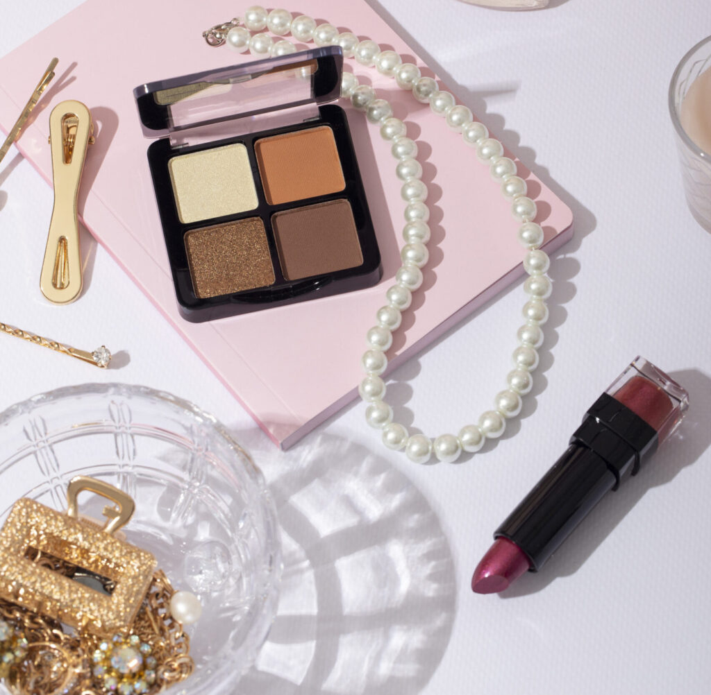 an aesthetic picture where lipstick , pearl jewellery , eyeshadow palette , a notebook , hairpin showing